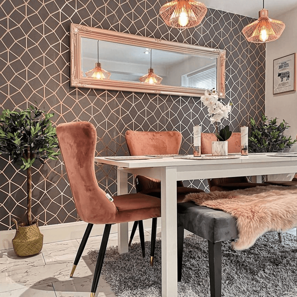 Pink velvet dining chairs and a bench at a white table against geometric wallpaper