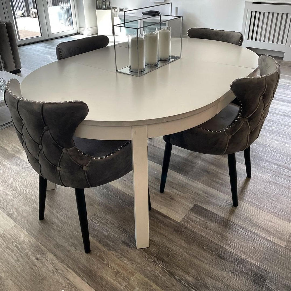 Dark grey button-back velvet chairs with studded trim around a white oval table