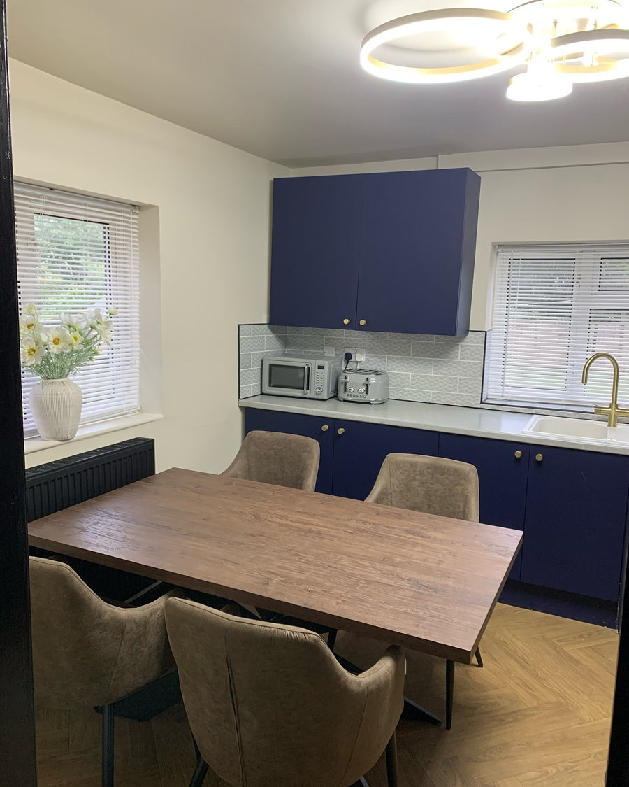 Walnut dining table with taupe dining chairs in a navy blue kitchen